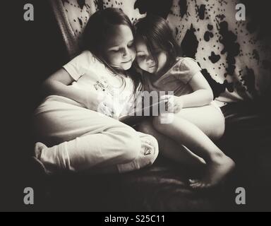 Schwarz-weiß Bild von zwei Schwestern sitzen zusammen an einem Tablet-PC suchen Stockfoto