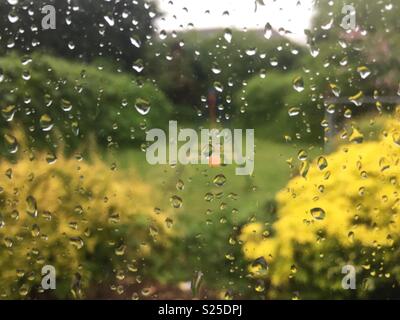 Regentropfen auf ein Fenster mit Blick auf einen Garten mit Schaukel eines Kindes sichtbar. Stockfoto