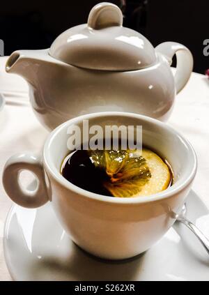 Weisse Teekanne, Tasse und Untertasse mit schwarzen Tee und Zitrone. Stockfoto