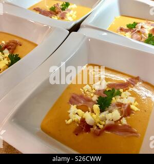 Salmorejo - Traditionelle spanische Suppe mit Tomaten, Knoblauch, Brot und Serano Schinken und Eier toping in eine rechteckige weiße Schüssel. Mehrere Suppenschüsseln. Stockfoto