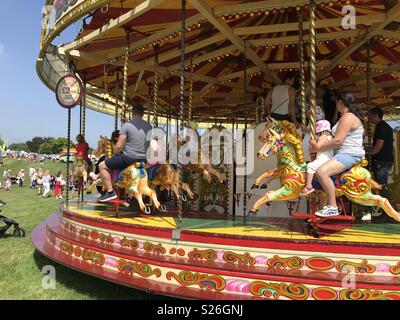 Eltern und Kinder genießen eine Fahrt auf einem Jahrmarkt an einem sonnigen Sommertag. Stockfoto