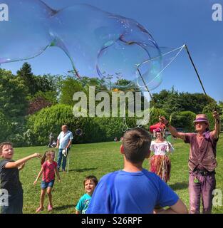 Mann und Frau riesige Seifenblasen, unterhaltsam eine Gruppe von Kindern, Sherborne Castle Country Fair, Sherbourne, Dorset, England Stockfoto