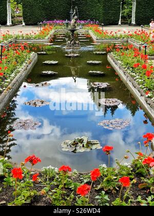 Roten Geranien Surround formalen architektonischen Teich von italienischen Garten mit Wider bewölkten Himmel und klassische Brunnen in den Butchart Gardens in Victoria BC Stockfoto