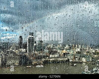 Regen auf dem Fenster der Shard, London, UK, über die Themse in Richtung Fenchurch Street und über die Stadt. Ein Regenbogen der Himmel leuchtet wie die Sonne durch Brüche, beleuchtet die Stadt unten. Stockfoto