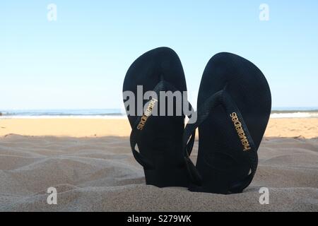 Flipflops stecken im Sand am Strand. Stockfoto