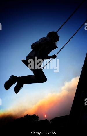 Mädchen in der Silhouette auf Swing gegen die untergehende Sonne Stockfoto