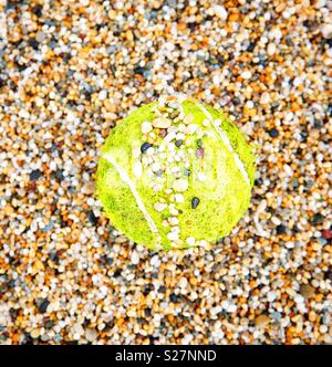 Ein gelber Tennisball auf einem Kies Hof in kleinen Steinchen in einem grass roots Sport Bild abgedeckt Stockfoto