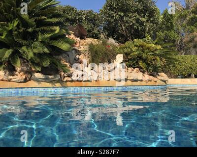 Schwimmbad und Steingarten mit einem Sago Palm (Cycas Revoluta) und eine römische Büste, die in einem mediterranen Garten, Low Angle View Stockfoto