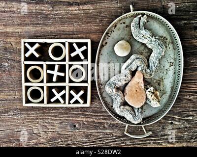 Nullen und Kreuze oder Tic-tac-toe Kinder spiel Neben einem dekorativen Fach von Objekten auf eine körnige Tischplatte. Kreuze zu gewinnen. Stockfoto