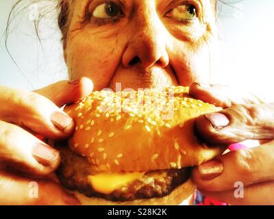 Ältere Frau essen Käse Burger Stockfoto