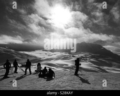 Schwarze und weiße Silhouette der Skifahrer und Boarder auf dem Berg vor der untergehenden Sonne Stockfoto