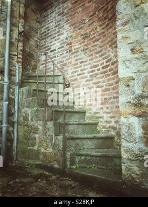 Treppen ins Nirgendwo. Eine alte, verwitterte Treppe mit moosbedeckten Stufen und einem Handlauf aus Metall führt hinauf und in eine Ziegelmauer, nirgendwo hin Stockfoto