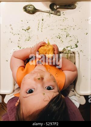 Ansicht von oben, für ein Baby Mädchen sitzen in einem Hochstuhl essen einen Pfirsich. Stockfoto