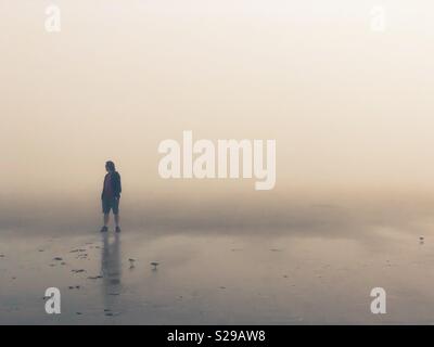 Ein Mann, der allein stehend auf einem nebligen Strand. Stockfoto