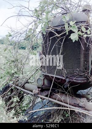 Blass vintage Filter auf das Foto der Vorderachse von Vintage verrosteten Traktor und Grill, mit Reben bewachsen, sitzen in Bauernhof Feld Stockfoto