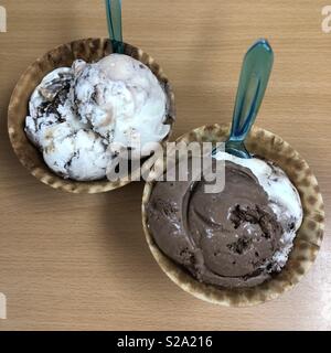 Zwei Waffel Schüsseln mit cremige Schokolade und Eis gefüllt, mit blauem Kunststoff Löffel Stockfoto
