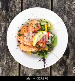 Auf der Suche nach unten von oben auf eine Fischplatte mit frischen Garnelen in ihren Schalen und Salat in einem Restaurant Stockfoto