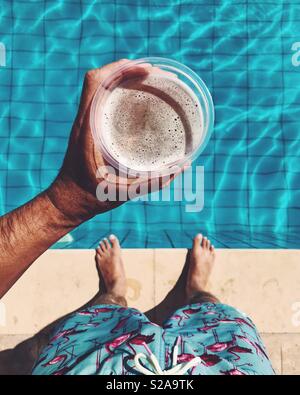 Sie betrachten eine Hand mit einem Pint Bier über einen Swimmingpool Stockfoto