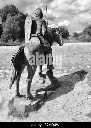 Vorwärts in die Schlacht (Holz Skulptur eines normannischen Soldaten zu Pferd, an der Stelle der Schlacht von Hastings, mit Battle Abbey im Hintergrund) Stockfoto