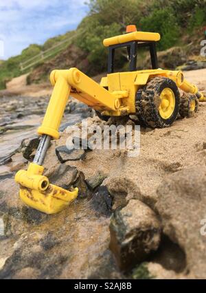 Child's digger Spielzeug in Sand und Wasser stellen auf einem Strand in voller Größe unter Anwendung von Zwangsarbeit, Perspektive Technik zu schauen. Rock Beach, Cornwall. Stockfoto