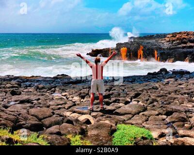 Gebräunte mann Arme ausgestreckt, die frische heiße Lava aus Göttin Pele fließt in die stürmischen Wellen unten auf der Insel von Hawaii Stockfoto