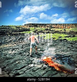 Mann laufen bergauf ausbrechenden mit geschmolzener Lava in Hawaii unter Teilweise bewölkt blauer Himmel Stockfoto