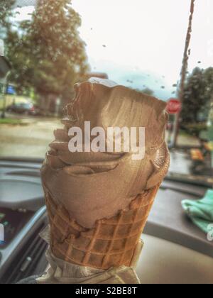 Weiche Schokolade dienen Eis in der Waffel Kegel. Es wird an einem regnerischen Tag im Auto genossen. Regentropfen auf der Windschutzscheibe, und ein Stop-Zeichen kann in der Ferne zu sehen ist. Stockfoto