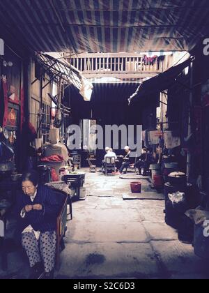 Alte chinesische Frau entspannt als Karte Spiele läuft im Hintergrund in einer ruhigen Seitenstraße am Pingyao, Shanxi Province, China Stockfoto