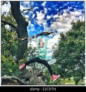 Ein junger Spaß Mädchen schwingen in einem Baum. Stockfoto