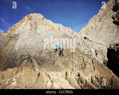 Ein Mann wird gesehen, Klettern auf einer Felswand in Three Cliffs Bay auf die Gower Halbinsel in Wales. Stockfoto