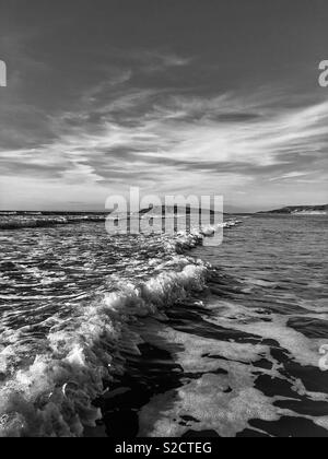 Welle brechen auf llangennith Strand, Gower, Wales, Oktober, mit Burry Halligen in der Ferne. Stockfoto