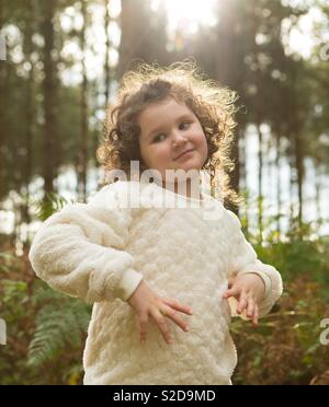 Schöne lockige blonde junge Mädchen in der Sonne im Wald Wald in Cannock Chase, Staffordshire stand. Stockfoto