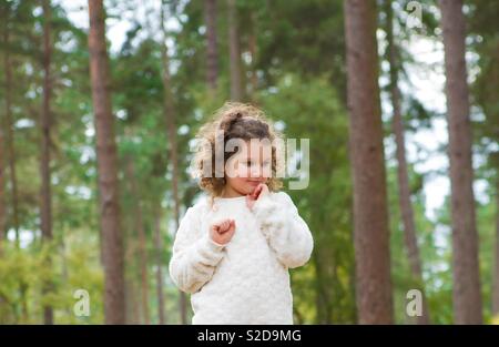 Engelhaftes lockigen Haaren junge Mädchen stand Denken in Wald Wald in Cannock Chase. Kind stand vor der Bäume eine weisse Spitze. Unschuldige Kind. Stockfoto