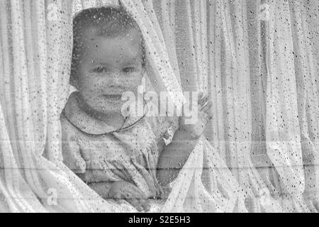 Kleines Mädchen im Fenster an regnerischen Tag Stockfoto