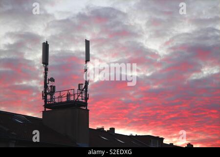 Dach mit mobilen Masten und Antennen in bunten Sonnenuntergang und roten Wolken Stockfoto