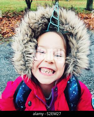Porträt eines lächelnden 6 Jahre altes Mädchen mit Unicorn horn Stirnband und rosa Winter Mantel mit pelzigen Haube Stockfoto