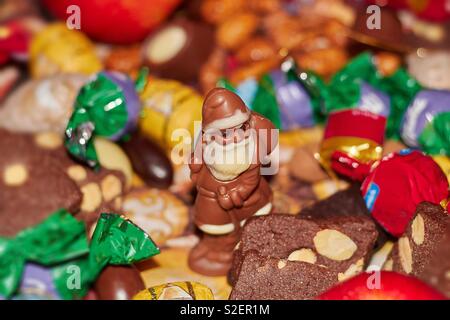 Ein Weihnachtsmann aus Schokolade mit Sack und Spazierstock wandert durch eine bunte Platte mit Süßigkeiten, Lebkuchen, Kekse und Schokolade Bonbons in der Weihnachtszeit Stockfoto