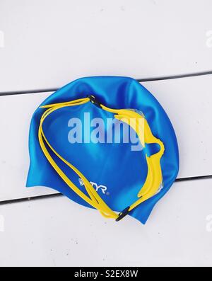 Schwimmen Notwendigkeiten. Blaue Badekappe und gelbe Brille auf einer weißen Bank. Am 1. Juli 2018 Stockfoto