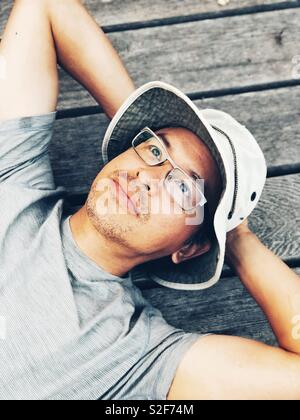 Im mittleren Alter asiatischer Mann mit Wanne Hut und Brille suchen Festlegung auf Camping Plattform in der kanadischen Wildnis Stockfoto