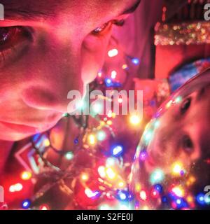 Kleiner Junge sieht auf seine Reflexion in einem Christbaumschmuck. Stockfoto