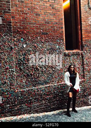 Junge Frau blasen Bubble Gum für Foto opp vor Gummi abgedeckt Wand in Post-Gasse in Seattle. Stockfoto