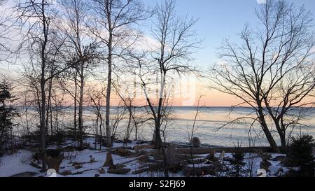 Pastellfarben Dämmerung über Lake Superior mit Silhouettiert Bäume und Schnee auf Shoreline in Vordergrund Stockfoto