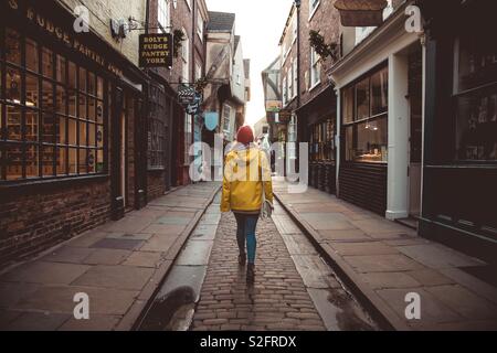 Eine Ansicht der Rückseite eine modische junge Mädchen zu Fuß entlang einer historischen mittelalterlichen Straße wie das Chaos in der historischen Stadt York UK bekannt Stockfoto