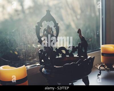 Indische Gottheit Lord Ganesha - Elefanten Gott - durch 2 Kerzen auf der Fensterbank an einem indischen Haushalt in Großbritannien flankiert. Stockfoto