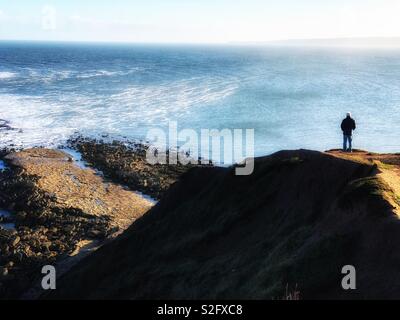 Mann steht auf einer Klippe mit Blick auf das Meer Stockfoto