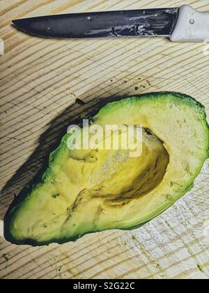 High Angle Shot eine halbe Avocado auf Schneidebrett mit Messer Stockfoto