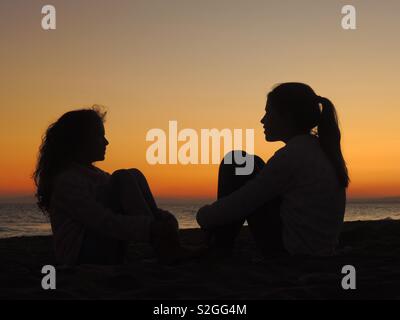 Schwestern beobachten Sonnenuntergang Silhouetten Stockfoto