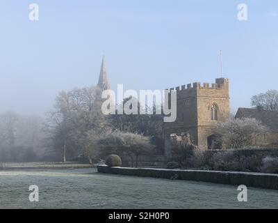 Broughton Schloss Torhaus mit Pfarrkirche Turm gegen einen schönen blauen Himmel umrahmt und in einer Winterlandschaft nach dem härtesten Frost des Jahres. Stockfoto