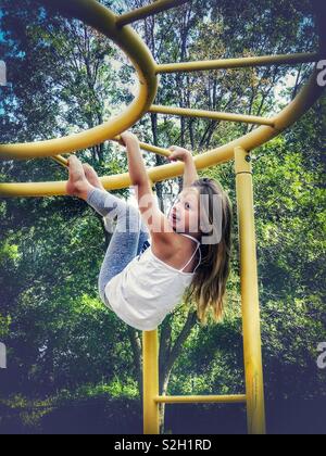 Kleines Mädchen, ein lustiges Gesicht hängend von Monkey Bars Stockfoto