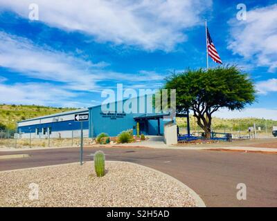 Titan Missile Museum, Shauarita, Arizona. Metall Gebäude mit Bürgersteig, Auffahrt und Wüste Landschaft unter blauem Himmel mit flauschigen weissen Wolken. Grüner Baum und Amerika Flagge. Stockfoto